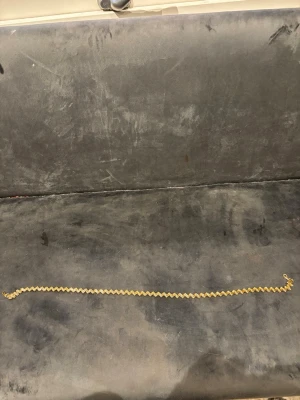 Guldfärgat kedjehalsband i zickzack - Säljer ett snyggt halsband i guldfärg med zickzack-formad kedja. Halsbandet har en klassisk karbinhake och är tillverkat i metall. Perfekt för dig som gillar stilrena och trendiga accessoarer.