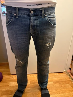 Dondup Luxury Denim Jeans - Slim Fit - Made in Italy - Selling a pair of premium Dondup jeans in a stylish medium blue wash. Dondup is known for their high-quality Italian craftsmanship and perfect fit.  These jeans feature a contemporary look with factory-made distressed details (small rips) on the front for a rugged yet refined aesthetic. They have only been worn a few times and are in excellent condition.  Brand: Dondup  Origin: Made in Italy  Color: Medium Blue  Details: Button fly, distressed detailing, premium denim feel. Size: 32