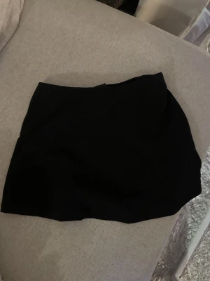 Svart kortkjol i enkel design -  sopren svart kortkjol med rak passform och minimalistisk look. Kjolen är utan synliga detaljer och passar perfekt till många olika stilar. Perfekt basplagg för garderoben.