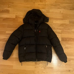 Svart pufferjacka från Polo Ralph Lauren - Svart pufferjacka från Polo Ralph i storlek L. Perfekt nu till det kalla vädret!Använd endast 1 gång och säljer pga för liten på mig. Köpt för 5999kr/ mitt pris 2700kr. Priset är ej hugget i sten och tveka inte på att ställa frågor!