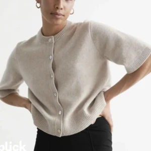 Other stories kofta  - Säljer en stilren beige kofta med korta ärmar och knappar framtill. Perfekt för lager-på-lager och passar till många olika outfits. Ribbstickade detaljer vid ärmslut och nederkant ger en fin finish.