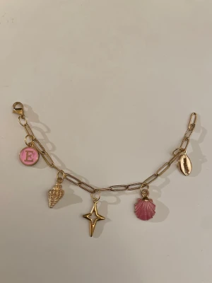 Guld berlockarmband  - Snyggt guldigt armband med 4 berlocker: snäcka, stjärna, rosa snäckskal och ett guldigt snäckskal. Kedjan är i rostfritt stål.                               Tveka inte fråga om du har flera frågor 🌸💕