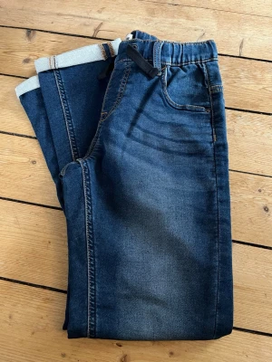Blå jogger jeans med snörning - Snygga blå jogger jeans från JOGGER JOEY i storlek 158. Jeansen har resår och snörning i midjan för extra komfort och en avslappnad look. Klassisk modell med mjukt denimtyg. Aldrig använda