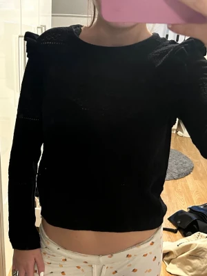 Svart stickad tröja med volang - Trendig svart stickad tröja med volangdetaljer på axlarna och genombrutet mönster. Långärmad och något croppad modell som ger en cool siluett. Knappt använd! Vet inte vart tröjan är ifrån men det står stories på lappen💓