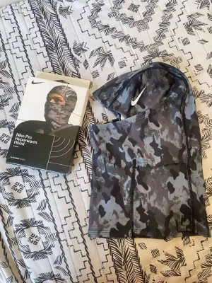Nike Pro Shiesty Hyperwarm Hood camo - Nike Pro Shiesty Hyperwarm Hood i grått och svart camo-mönster. Tight passform med stretchigt material och vit Nike-logga framtill. Perfekt för träning utomhus när det är kallt. Säljes med originalförpackning.
