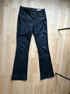 Svarta bootcut jeans med hög midja - Snygga svarta läderbyxor med bootcut passform. Klassisk femficksmodell med knapp och dragkedja fram. Byxorna är mjuka och stretchiga. De är i storlek S och längd 30. 