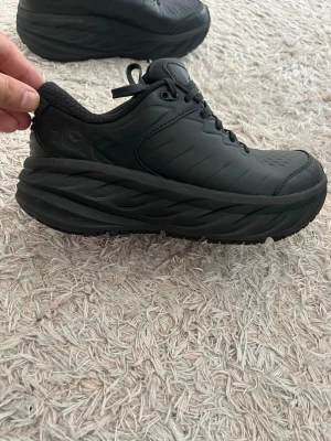 Svarta sneakers från Hoka One One - Nypris 2400kr. Oanvända. Tjocka svarta sneakers från Hoka One One med hög plattformssula och snörning. Skorna har en rund tå och är tillverkade i syntetmaterial med slitstark yttersula. Perfekta för dig som gillar chunky sneakers och vill ha maximal komfort.