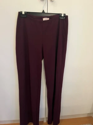 Mörkröda byxor - Snygga mörklila byxor från Nelly med vida ben och låg midja. Byxorna har en minimalistisk design utan synliga fickor eller detaljer och är tillverkade i ett mjukt material som känns bekvämt hela dagen.sitter tajt på som inte syns på bilden