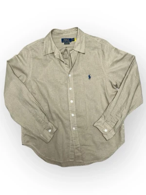 Polo Ralph Lauren Skjorta - Stilren skjorta i neutral beige ton. Enkel att matcha och perfekt året runt. OBS: Löngden på tröjan är ganska kort för o vara M, antar det är unisex eller kvinnliga modellen. Materialet är kanske linnen Skick: 8/10 Pris kan diskuteras 📦 Skickas eller möts upp