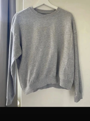 Grå sweatshirt från 157 - En basic grå sweatshirt från 157 med rund halsringning och ribbade muddar vid ärmslut och nederkant. Perfekt för en avslappnad och stilren look.😊