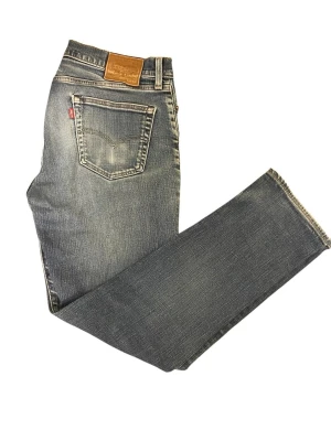 Levi's blå raka jeans - Klassiska blå jeans från Levi's med raka ben och snyggt slitna detaljer. Jeansen har fem fickor, läderpatch bak och den ikoniska röda Levi's-taggen. Tillverkade i bomullsdenim för en skön och avslappnad look.