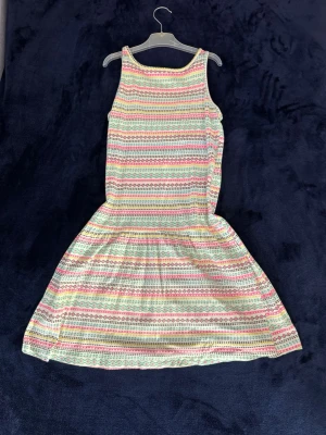 Mönstrad sommarklänning - Söt kortklänning med färgglada ränder i färgerna rosa, blått, gult och grönt. Barnstorlek 152. Klänningen är ärmlös och har en avslappnad passform. Perfekt för varma dagar. Tillverkad i mjuk bomull som känns skön mot huden.