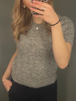 Grå stickad t-shirt Gina Tricot - Säljer en grå, kortärmad stickad t-shirt från Gina Tricot. Tröjan har rund halsringning och är gjord i ett mjukt, melerat garn som ger en mysig känsla. Perfekt att styla med jeans eller kjol för en enkel men snygg look.