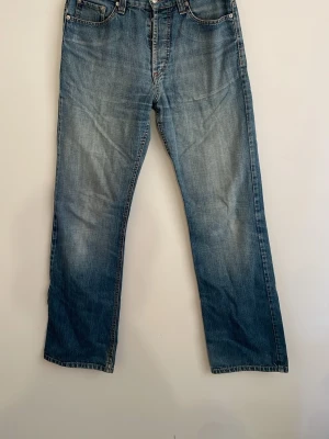 Blå raka jeans med klassisk tvätt - Ett par blå jeans med rak passform och klassisk ljus tvätt. Jeansen har fem fickor, bälteshällor och dragkedjegylf. Perfekta för en avslappnad och tidlös stil. Materialet är denim i bomull.