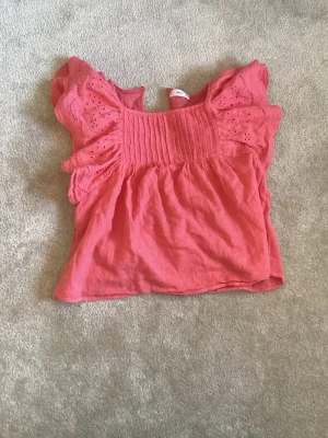 Coralrosa blus med volangärmar - Söt coralrosa blus med volangärmar och ribbad detalj över bröstet. Luftig och skön 💕