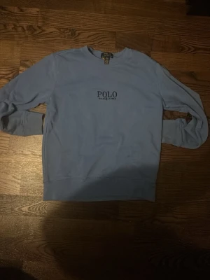 Blå sweatshirt från Polo Ralph Lauren - Snygg ljusblå sweatshirt från Polo Ralph Lauren med broderad logga på bröstet. Tröjan har rund halsringning, långa ärmar och ribbade muddar. Perfekt för en avslappnad och stilren look.