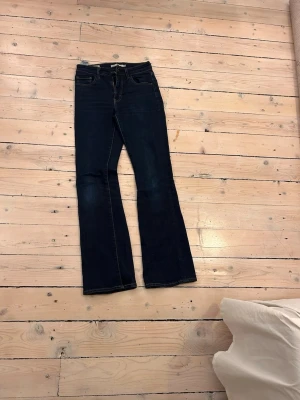 Levi's 725 High Rise Bootcut Jeans - Mörkblå bootcut jeans från Levi's, modell 725 High Rise Bootcut. Jeansen har hög midja, klassiska fem fickor och kontrastsömmar. Tillverkade i slitstarkt denim med snygg passform som framhäver benen. Det är inte fri frakt 