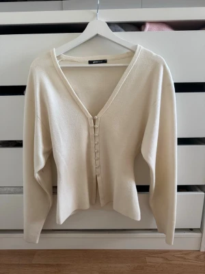 Krämvit kofta från Gina Tricot - Snygg krämvit kofta från Gina Tricot med v-ringning och knappar framtill. Långärmad modell i mjukt material som ger en clean och stilren look. Perfekt att matcha med jeans eller kjol för en enkel men trendig outfit.