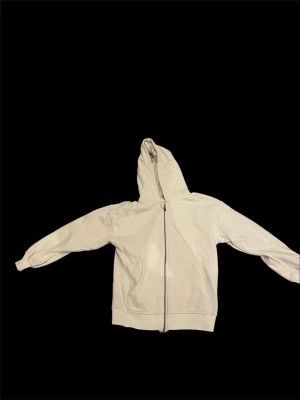 Beige ziphoodie med fickor - Snygg beige hoodie med dragkedja framtill och två stora fickor. Klassisk modell med luva och ribbade muddar vid ärmslut och nederkant. Perfekt för en avslappnad streetstyle-look. Storlek 146-152