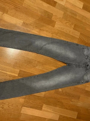 Grå slim fit jeans W29 L32 - Snygga grå slim fit jeans med klassisk femficksdesign och diskreta slitningar på låren. Jeansen har smal passform och raka ben, perfekta för en stilren och modern look. Materialet är mjukt och stretchigt för extra komfort.