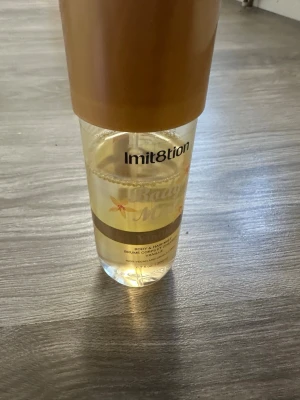 Imitation Vanilla Body & Hair Mist - Fräsch body & hair mist från Imitation med doft av vanilj. Flaskan är genomskinlig med guldfärgat lock och detaljer. Innehåller 200 ml och är vegansk samt cruelty free. Perfekt för dig som älskar söta och mjuka dofter.