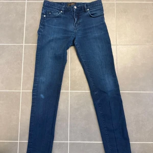 Blå slim fit jeans från J.Lindeberg - Snygga blå slim fit jeans från J.Lindeberg med klassisk femficksdesign och diskret logga på myntfickan. Jeansen har normal midja, dragkedjegylf och är tillverkade i ett mjukt denimtyg med lätt stretch för skön passform. Storlek 32/34