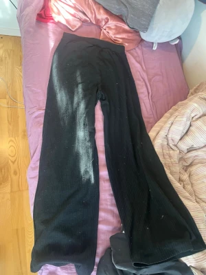 Svarta legings  som är ribbade  - Säljer ett par svarta mjukisbyxor med ribbad struktur och breda ben. Perfekta för chill dagar hemma eller när du vill ha en avslappnad stil. Byxorna har hög midja och är gjorda i ett mjukt, stretchigt material som känns skönt mot huden.