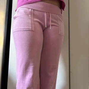 Rosa mjukisbyxor med fickdetaljer - Säljer ett par rosa mjukisbyxor med snörning i midjan och fickor med knappar bak. Perfekta för en avslappnad stil och superbekväma att ha på sig. Passar perfekt för mysiga dagar hemma eller en avslappnad dag ute. Ej använda,säljer om de på Plick för de var för korta. 