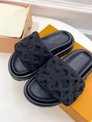 Svarta fluffiga slip-in sandaler - Svarta slip-in sandaler med breda, fluffiga band i mjukt tyg och präglat mönster. Sulan är svart och har en lätt upphöjd kant. Perfekta för att chilla hemma eller ute på stan.