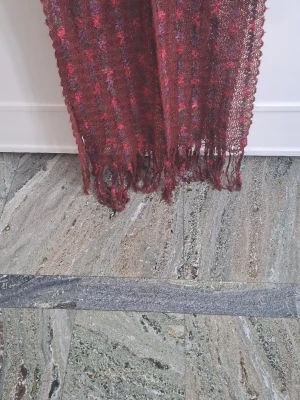 Vinröd sjal från Les 400 Coups - Säljer en vinröd sjal från Les 400 Coups med inslag av lila och rosa. Sjalen är stickad i ett tunt, luftigt material och har fransar längs kanterna. Perfekt att slänga över axlarna för en cool och bohemisk look.