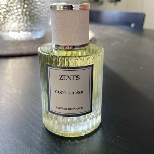 Zents Coco Del Sol Extrait de Parfum - Lyxig parfym från Zents i doften Coco Del Sol. Flaskan är genomskinlig med räfflad yta och har en silvrig kork med vit läderdetalj. Parfymen har en ljusgul nyans och ger en exklusiv känsla på hyllan. Endast ett sprut testat!