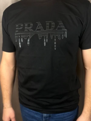 Svart  t-shirt med tryck - . T-shirten har rund hals och korta ärmar. Materialet ser ut att vara mjuk bomull, perfekt för en trendig och avslappnad stil.