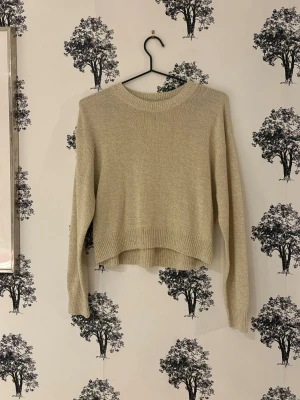 Beige cropped stickad tröja - Säljer en beige stickad tröja med croppad passform och rund hals. Tröjan har långa ärmar och ribbade muddar vid ärmslut och nederkant. Perfekt att styla med höga jeans eller kjol för en chill look.