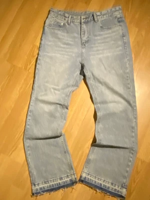 Flared Jeans - Ljus Blå - Säljer ett par ljusblå jeans med flare passform och trendig rå kant nedtill. Jeansen har klassisk femficksmodell och är tillverkade i denim. Perfekta för en avslappnad och cool stil.