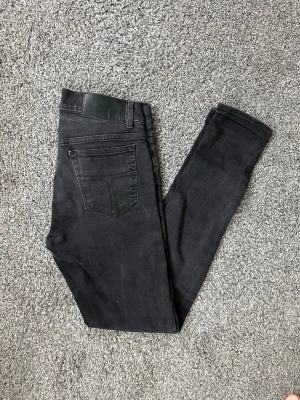 Svarta jeans från tiger of sweden - Snygga svarta  jeans med klassisk femficksdesign och diskreta sömmar. Jeansen har en smal passform och är tillverkade i ett stretchigt material som sitter tajt och bekvämt. Perfekta för en stilren och modern look.