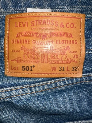 Svarta raka  jeans från Levi's, 501  - Säljer ett par Blå jeans från Levi's med klassisk rak passform. Jeansen har fem fickor, bälteshällor och en brun läderpatch bak i midjan. Tillverkade i slitstark denim som ger en cool och avslappnad look. Skriv om ni har frågor