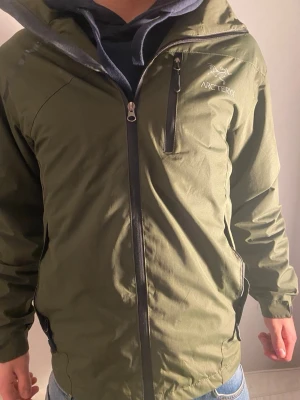 Grön vindjacka från Arc'teryx - Snygg grön vindjacka från Arc'teryx med dragkedja framtill, bröstficka med dragkedja och huva. Jackan har en sportig look och är perfekt för utomhusaktiviteter. Materialet är lätt och vindtätt, vilket gör den smidig att bära.Pris kan diskuteras mvh Melwin🙌