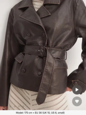 Brun skinnjacka från NA-KD - Snygg brun skinnjacka från NA-KD med klassisk krage, knappar och bälte i midjan. Jackan har långa ärmar och en stilren design som passar perfekt till många olika outfits. Nypris 999kr