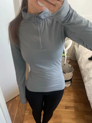 Blå långärmad träningströja - Slimmad blå långärmad träningströja med halv dragkedja och hög krage. Perfekt för löpning eller gym. Tröjan har en sportig look och är tillverkad i ett stretchigt funktionsmaterial som andas.