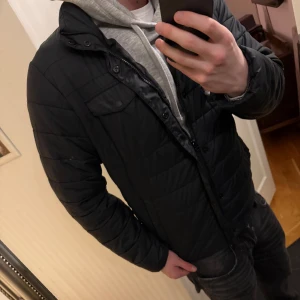 Svart pufferjacka från Levi's - Säljer en stilren svart pufferjacka från Levi's med klassisk krage och två bröstfickor med lock. Jackan har diskret röd Levi's-logga på bröstet och dragkedja framtill. Lättare jacka som tål kyla väl, perfekt nu de sista vintermånaderna och inför våren☺️ Skriv vid funderingar!