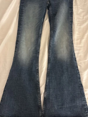 Blå utsvängda jeans från Weekday - Säljer ett par blå utsvängda jeans från Weekday med snygg slitning på låren. Jeansen har klassisk femficksdesign och är tillverkade i 79% bomull, 20% polyester och 2% elastan för en skön stretchig känsla.
