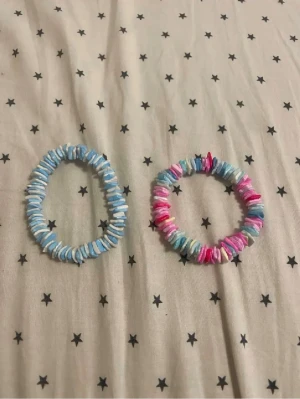 Två färgglada pärlarmband - Säljer två stretchiga armband med platta pärlor i pastellfärger. Ett armband är blått och vitt, det andra har mixade färger i rosa, blått och vitt. Perfekta för att addera lite färg till din stil. Gjorda av plast och elastisk tråd.