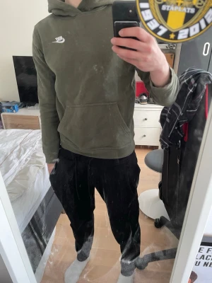 Olivgrön Nike hoodie med huva - Säljer en olivgrön hoodie från Nike med klassisk vit logga på bröstet. Hoodien har en stor magficka och justerbar huva. Tillverkad i mjukt bomullsmaterial och har ribbade muddar vid ärmslut och nederkant. Perfekt för en avslappnad och sportig stil.