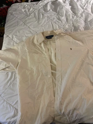 Gul skjorta från Ralph Lauren - Klassisk vit skjorta från Ralph Lauren med broderad logga på bröstet. Skjortan har lång ärm, knappar framtill och en avslappnad passform. Tillverkad i bomull och passar perfekt till en clean och stilren look.