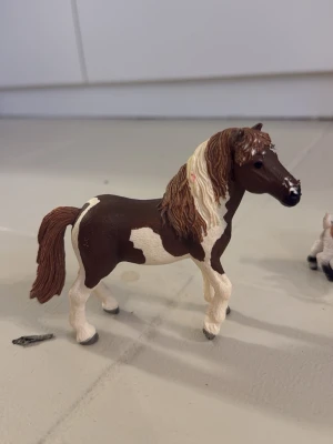 Blandade schleich djur - Säljer en realistisk hästfigur i plast med bruna och vita fläckar. Hästen har detaljerad man och svans i brunt och vitt, och står i en naturlig pose. Perfekt som leksak eller samlarobjekt för dig som gillar djur och hästar.