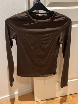 Brun långärmad topp från Lager 157 - En enkel och stilren brun långärmad topp från Lager 157. Modellen är figurnära med rund halsringning och tillverkad i ett mjukt, stretchigt material som känns bekvämt mot huden. Perfekt att matcha med jeans eller kjol för en clean look.