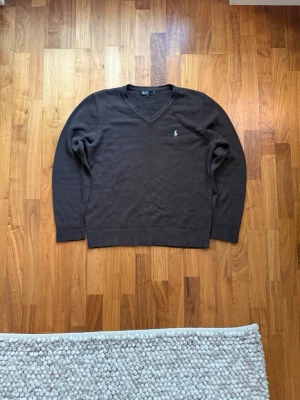 Ralph Lauren sweatshirt - Mörkbrun stickad tröja med V-ringning från Polo Ralph Lauren. Tröjan har en liten broderad logga i ljusblått på bröstet och ribbade muddar vid ärmslut och nederkant. Perfekt för lager-på-lager och en stilren look. Mycket bra skick, inga skavanker! Hör av er vid frågor eller funderingar!💬 snabb leverans🚚📦
