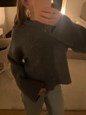 Mörkgrå stickad tröja med vida ärmar - Mysig mörkgrå/blå  stickad tröja med breda, vida ärmar och rund halsringning. Tröjan har en avslappnad passform och är perfekt för lager på lager. Materialet ser ut att vara mjukt och lite luddigt, vilket ger en skön känsla.