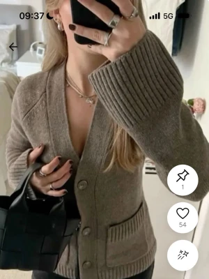 Beige kofta med breda ärmar - Mysig beige kofta med breda ribbstickade ärmslut och stora knappar framtill. Koftan har djup V-ringning och två fickor fram. Perfekt för lager på lager och enkel att styla till olika outfits.