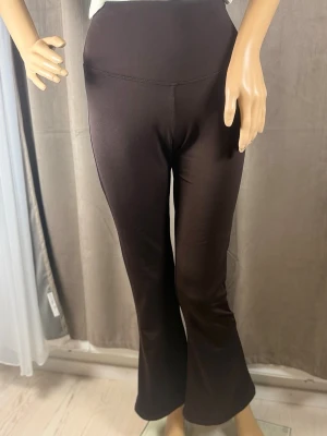 Bruna utsvängda mjukisbyxor - Mörkbruna mjukisbyxor med hög midja och utsvängda ben. Byxorna har en enkel, stilren design utan synliga fickor eller loggor. Tillverkade i ett mjukt och stretchigt material som ger en bekväm passform. Perfekta för en avslappnad och trendig look.